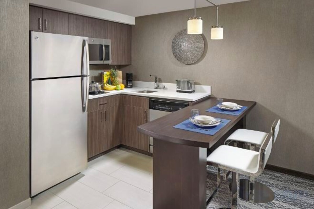 Una cocina moderna con refrigerador, microondas y lavavajillas integrados. Cuenta con una zona de comedor con mesa y sillas, y un adorno decorativo sobre el fregadero.