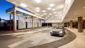 A modern hotel entrance with a car parked inside, featuring a covered walkway and decorative panels.