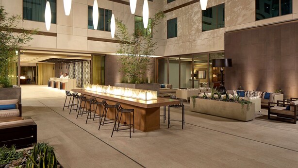 A spacious indoor lobby with a central bar area, seating arrangements, and a large plant.
