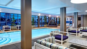 A poolside area with seating, a pool, and large windows offering a city view.