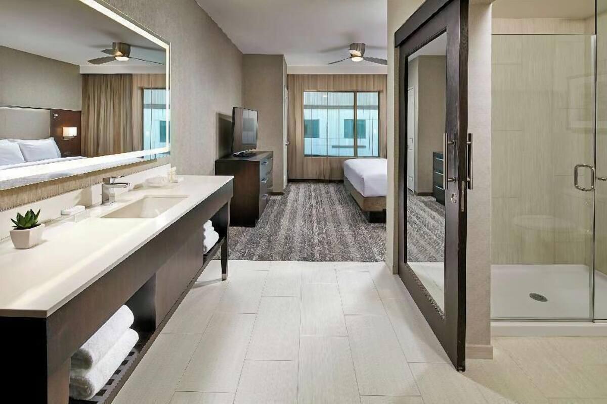 A hotel room with a large bathroom, a bed, a TV, and a shower.