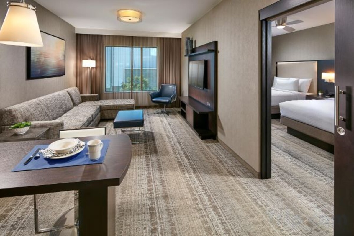 A hotel room with a sofa, a dining table with plates and cups, a TV, and a bed.