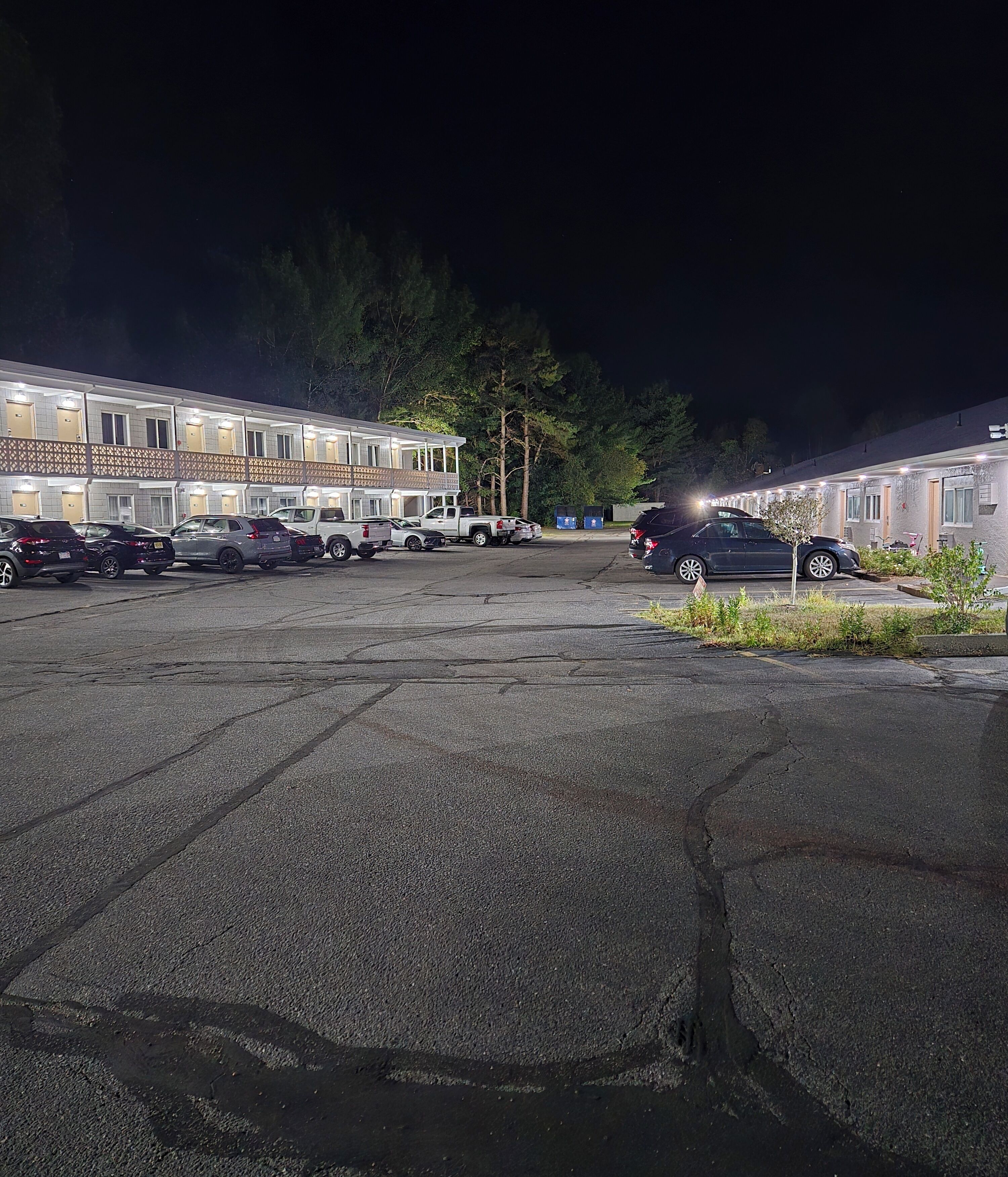 Un motel con varias habitaciones, un estacionamiento y un pequeño jardín.