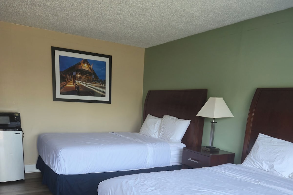 Ein Hotelzimmer mit zwei Betten, einer Mikrowelle, einem Nachttisch mit Lampe und einem Bild an der Wand.