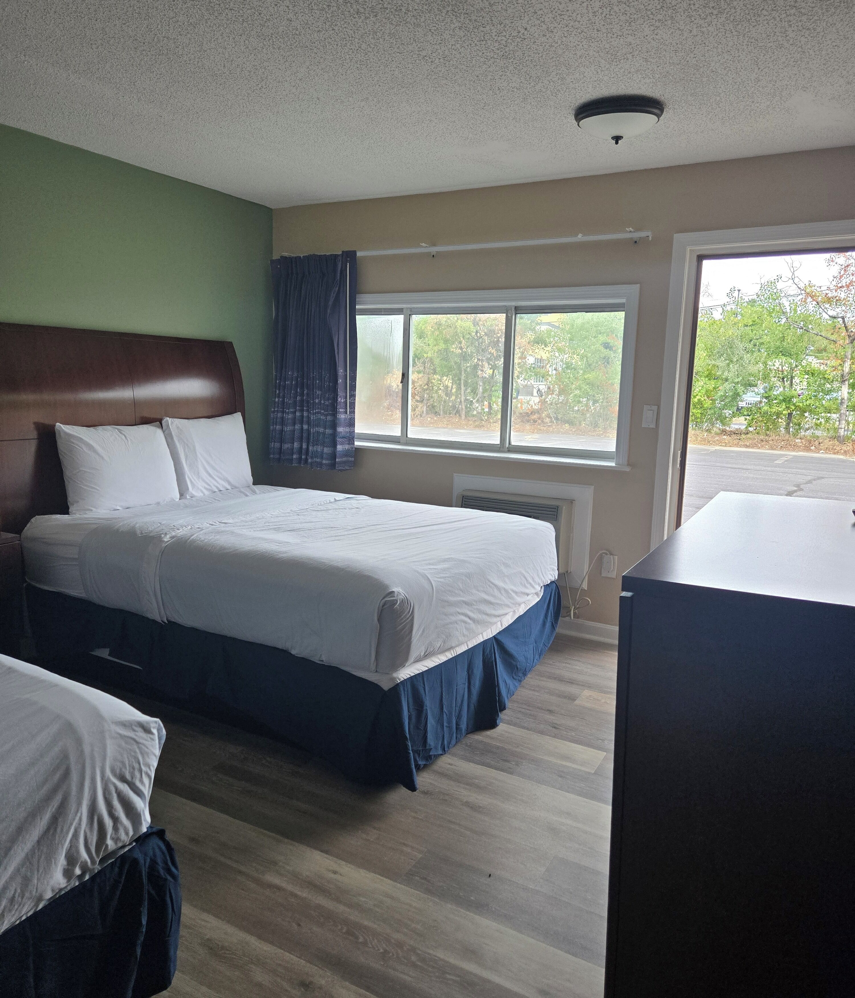 A hotel room with a bed, a desk, and a window with a view of trees and a parking lot.