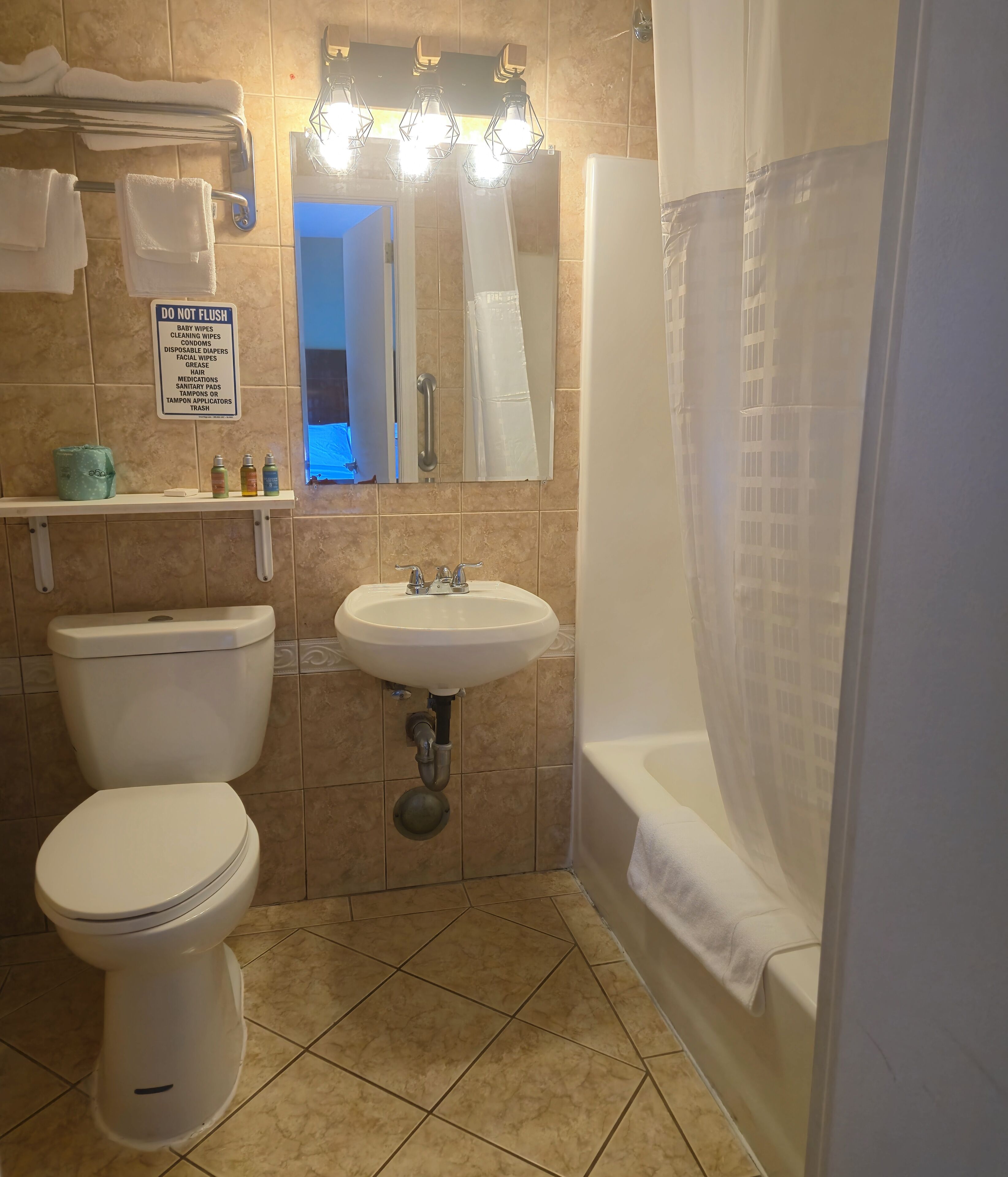 Baño con inodoro, lavamanos y zona de ducha. Un letrero indica qué no se debe tirar por el inodoro.
