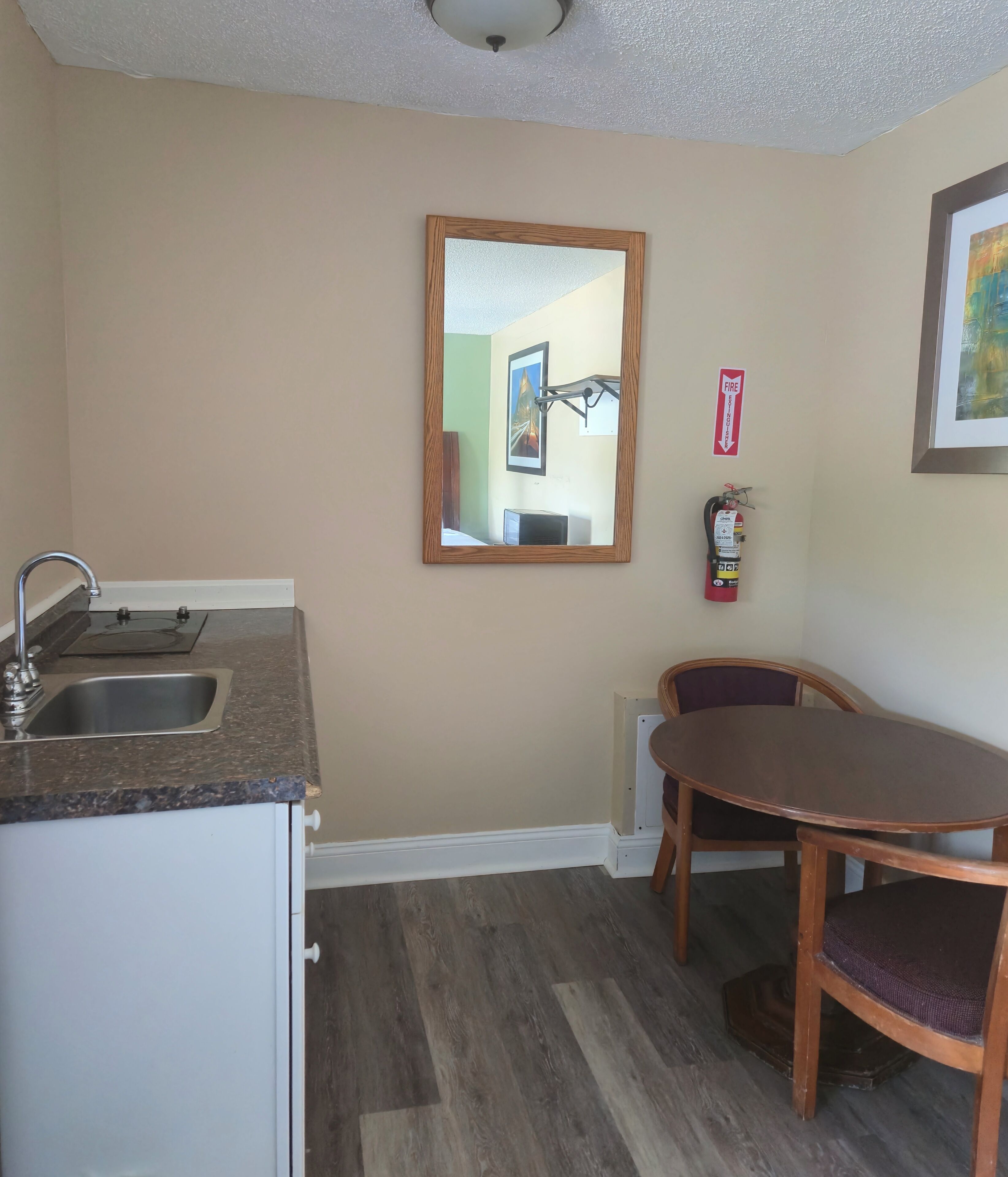 A compact kitchen with a sink, a wooden table, and a chair. A fire extinguisher is mounted on the wall.