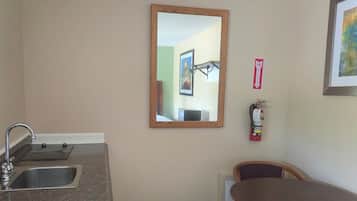 A compact kitchen with a sink, a wooden table, and a chair. A fire extinguisher is mounted on the wall.