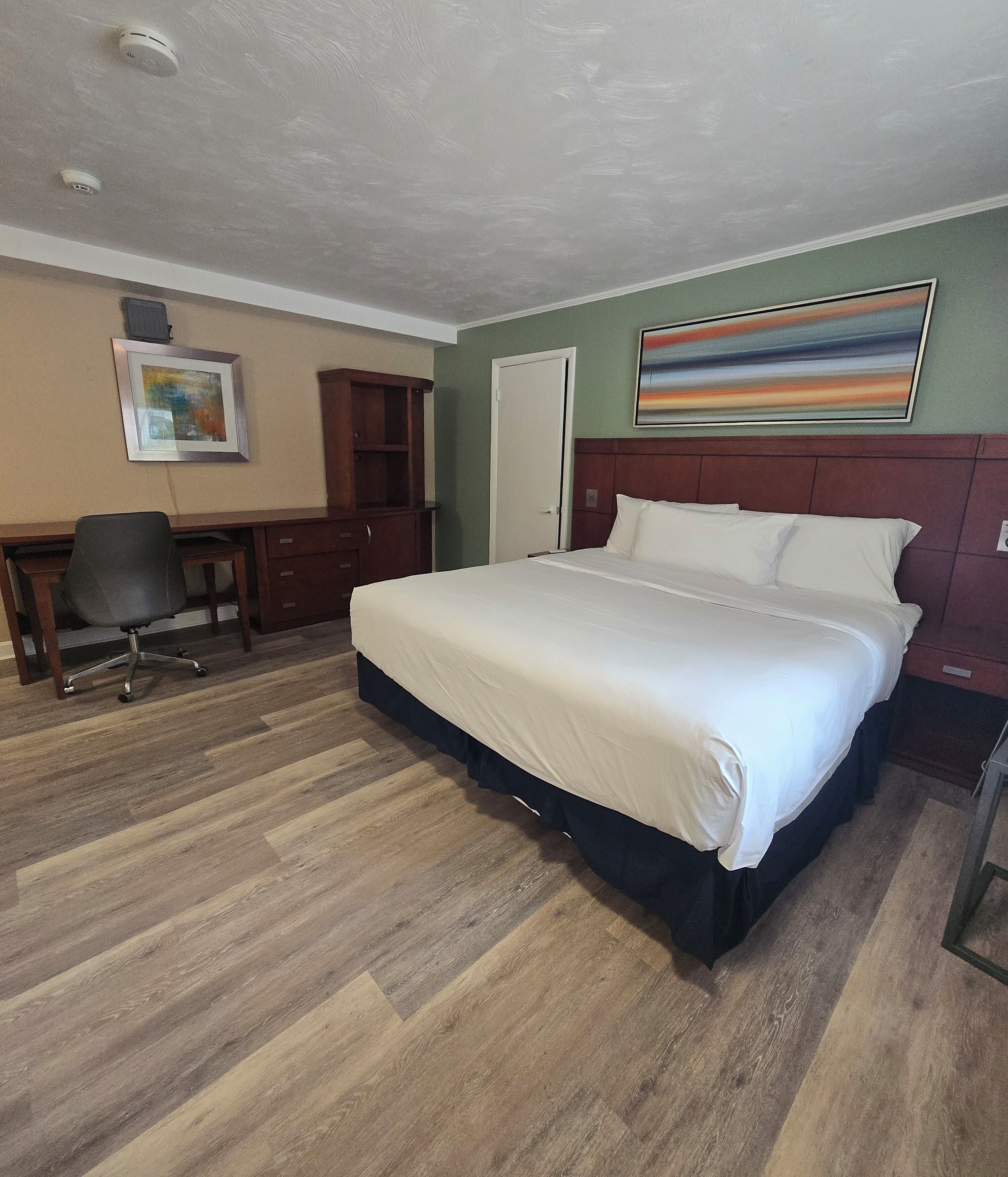 A hotel room with a large bed, a desk, a chair, and a painting on the wall.