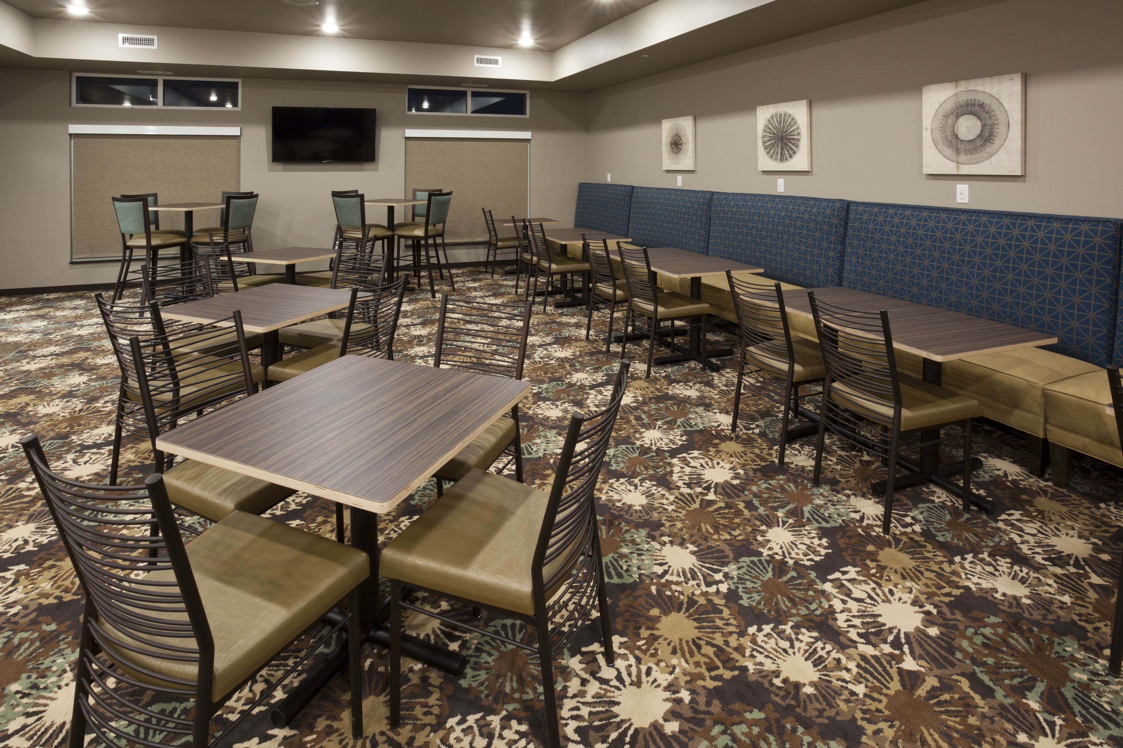 A conference room with multiple tables and chairs, a large screen, and a patterned carpet.