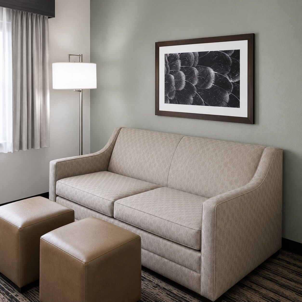 Habitación de hotel con sofá, dos otomanas, una lámpara de pie y una obra de arte abstracta enmarcada en la pared.