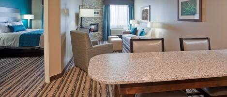 A hotel room with a bed, a desk, a chair, a dining table, and a view of the outdoors.