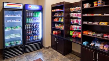 Un área de venta con refrigeradores de Pepsi y Doritos, estantes con snacks y un microondas.