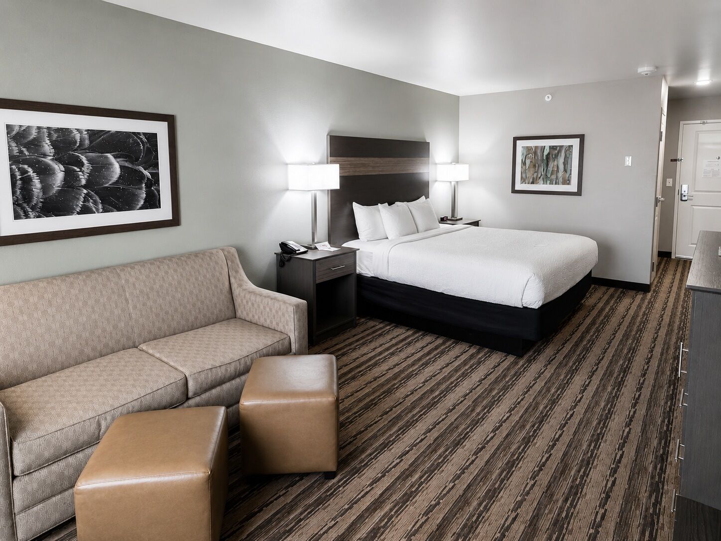 A hotel room with a bed, a sofa, a nightstand, and a lamp.