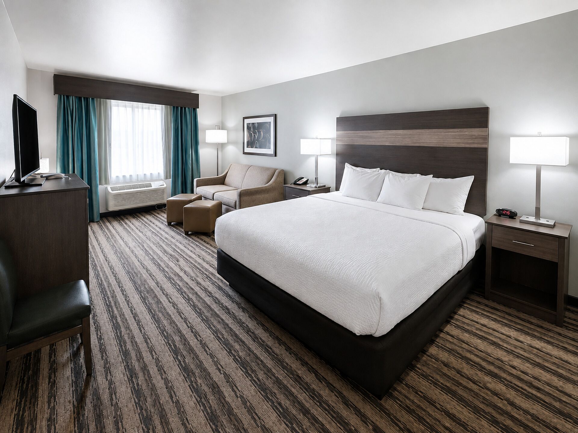 A hotel room with a large bed, a desk with a computer, a chair, a TV, and a window with curtains.