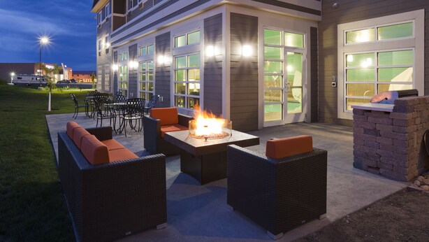 An outdoor patio area with wicker furniture, a fire feature, and a building with large windows and a garage. - GrandStay Hotel and Suites (Valley City)