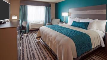 A hotel room with a large bed, a desk with a chair, a television, and a window with curtains.
