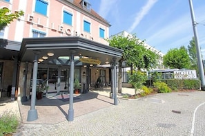 A hotel entrance with a covered waiting area, outdoor seating, and a clear sky.