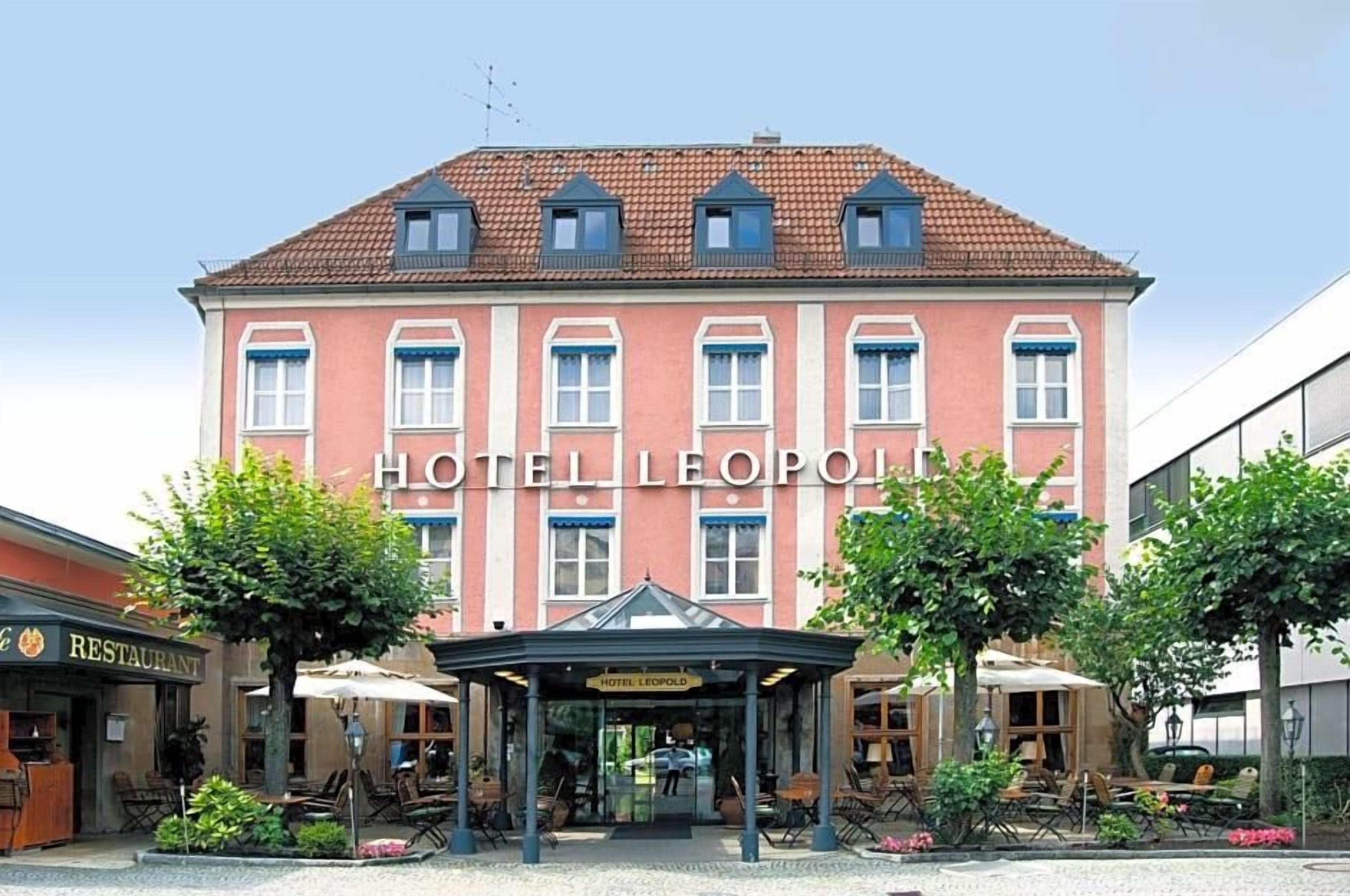 Ein Hotel mit roter Fassade, zahlreichen Fenstern und einem überdachten Eingangsbereich mit Außenbestuhlung.