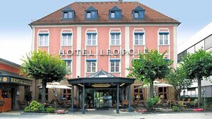 A hotel with a red facade, multiple windows, and a covered entrance area with outdoor seating. - Hotel Leopold (Munich)