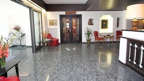 A lobby with a marble floor, red chairs, a reception desk, and a door leading to another room. - Hotel Leopold (Munich)