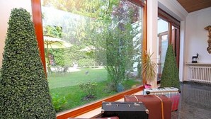 Een kamer met een groot raam, een verzorgd gesnoeid haagje en verschillende oude koffers.