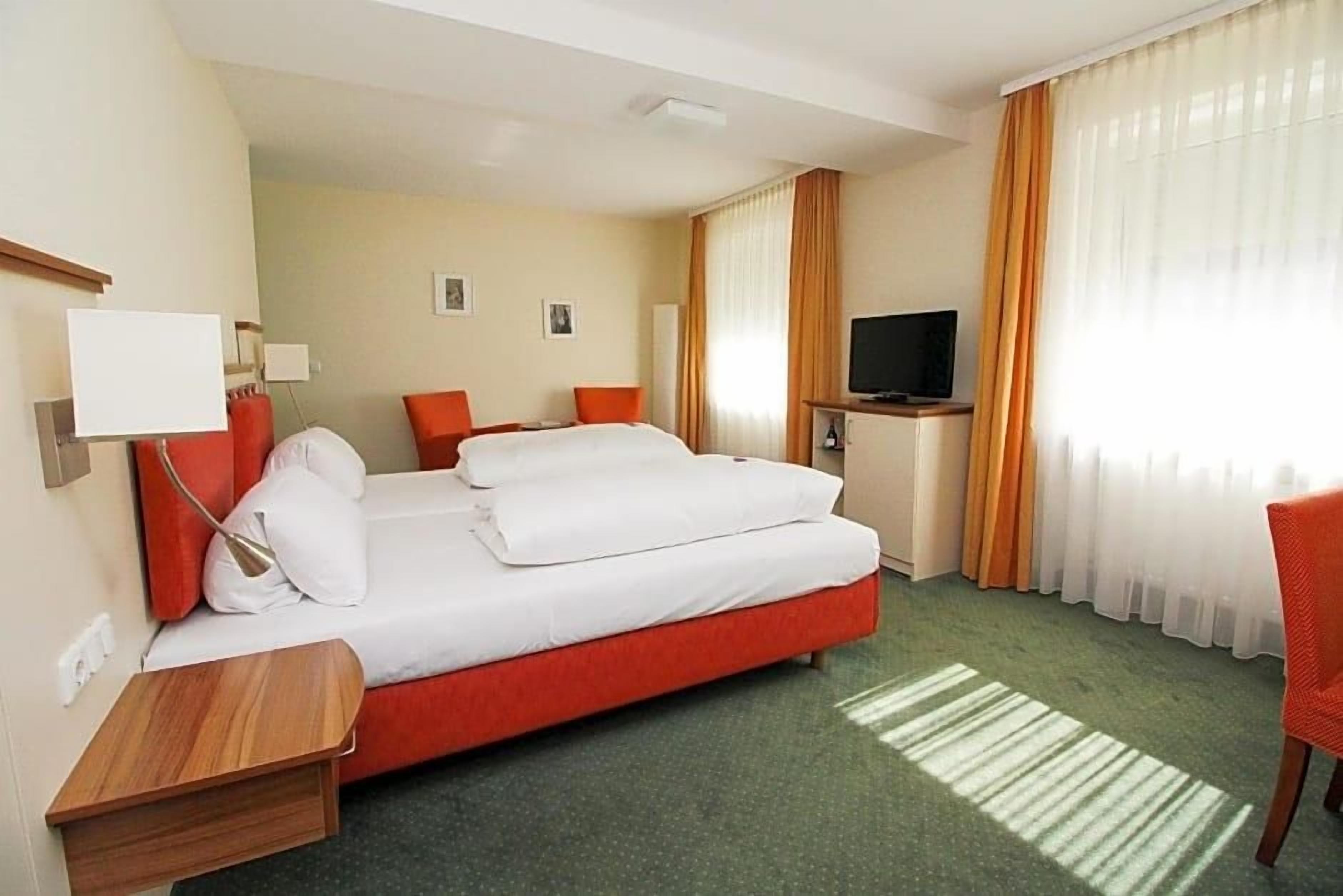 Ein Hotelzimmer mit Bett, Fernseher, Schreibtisch und Stuhl.