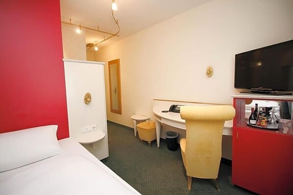 A hotel room with a bed, a desk, a chair, a TV, and a minibar.