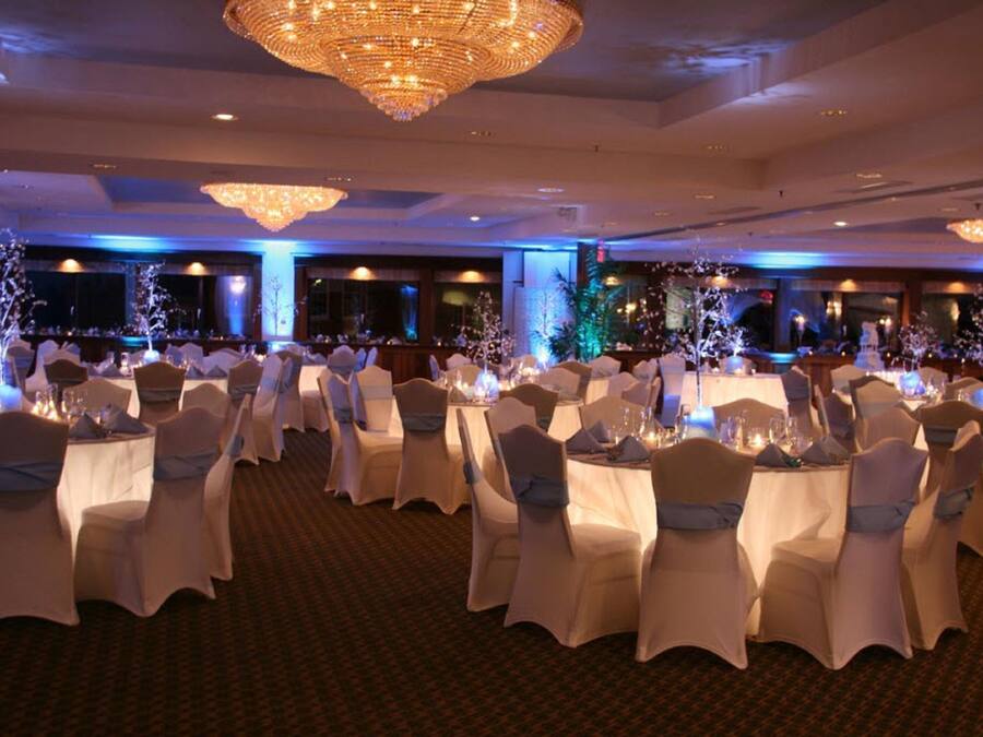 Une salle de banquet avec des tables rondes, des nappes blanches et des chaises ornées de rubans bleus.