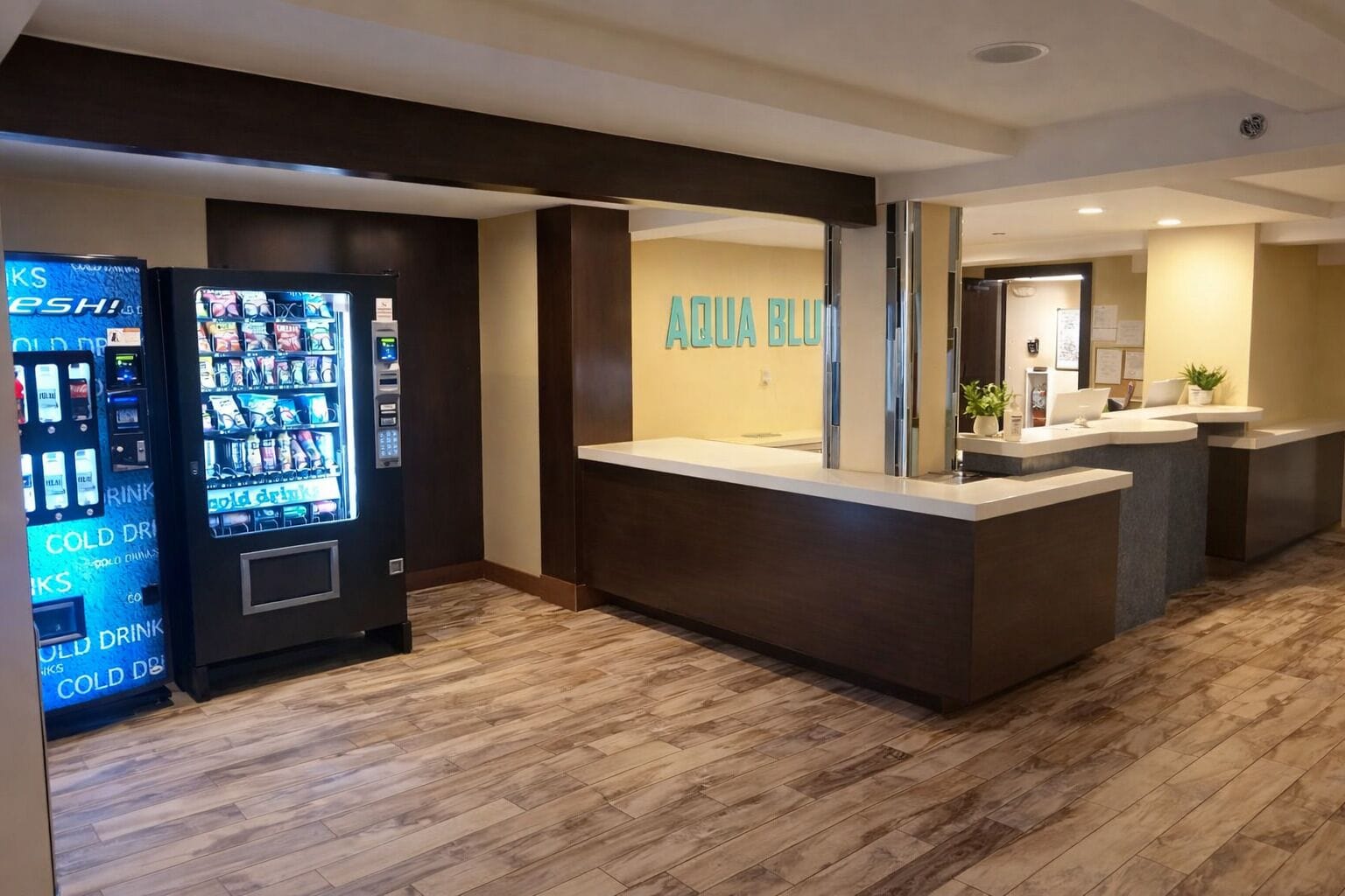 Un área de recepción con una máquina expendedora, un mostrador de recepción y una pared con el texto 'ARQUA BLUE'.