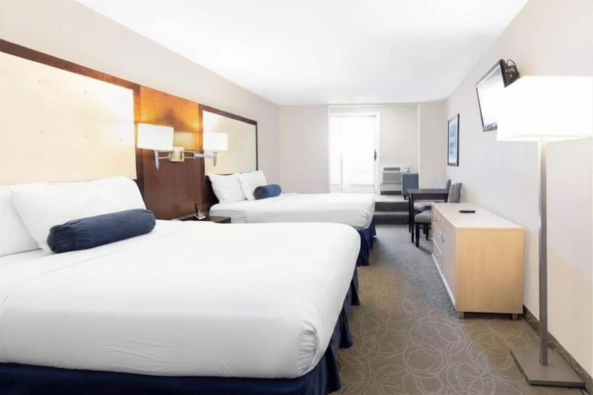 A hotel room with two beds, a desk, a chair, a lamp, and a television.