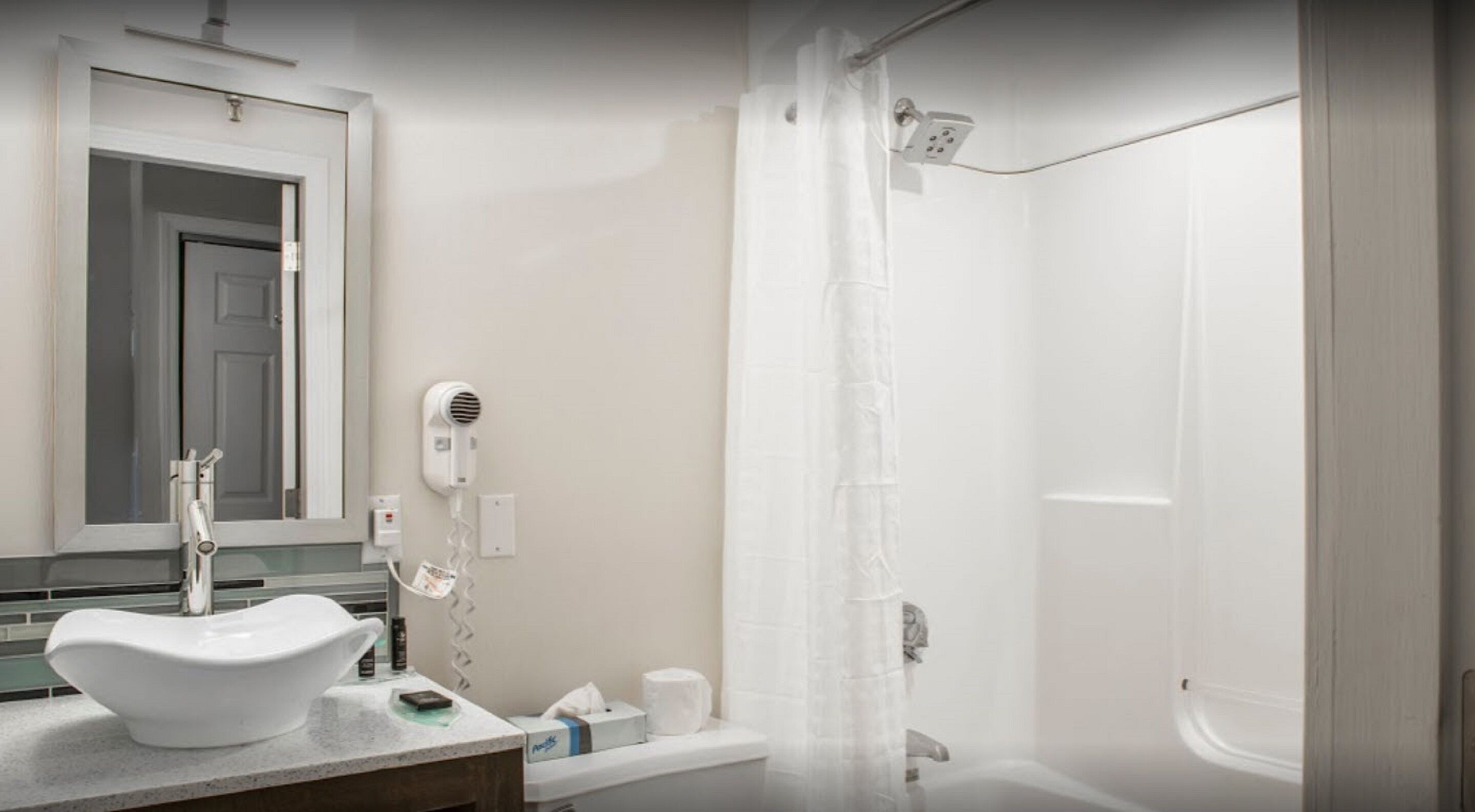 Een badkamer met een wit wastafelmeubel, een haardroger, een douchegordijn en een bad.