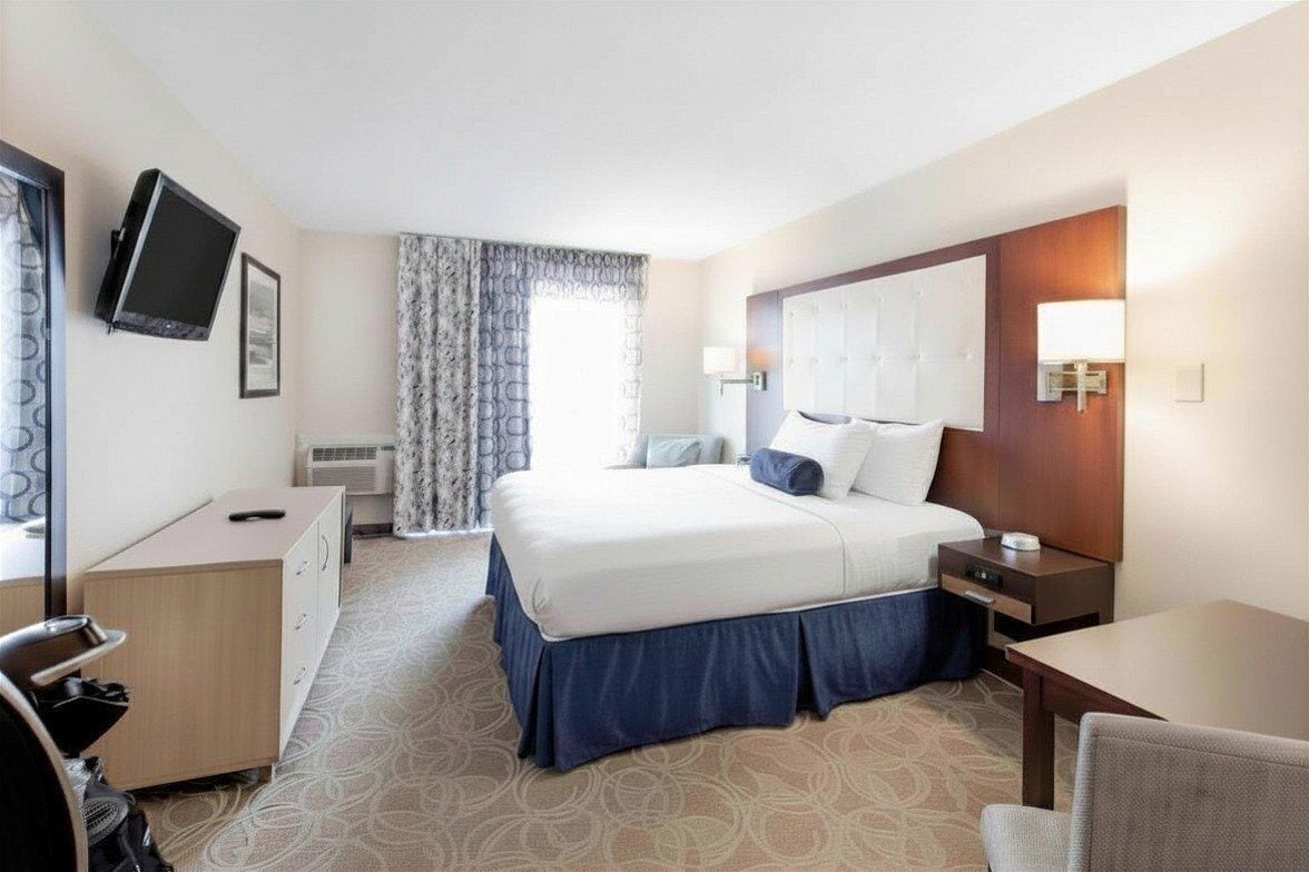 Une chambre d’hôtel équipée d’un lit, d’un bureau, d’une chaise, d’une télévision et d’une fenêtre avec des rideaux.