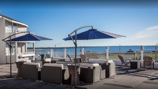 A deck with outdoor seating, a view of the ocean, and a building with a balcony. - Aqua Blue Hotel (Narragansett)