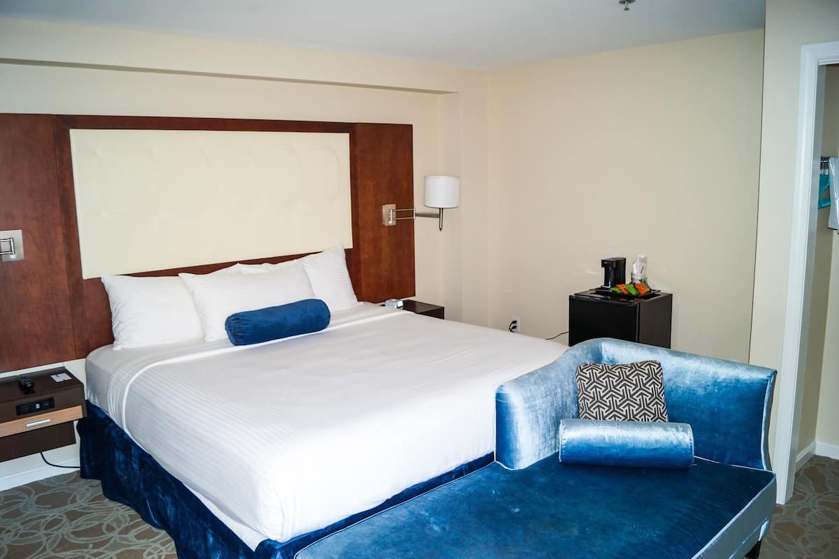 A hotel room with a large bed, a bedside table, a lamp, and a small side table with a decorative item.