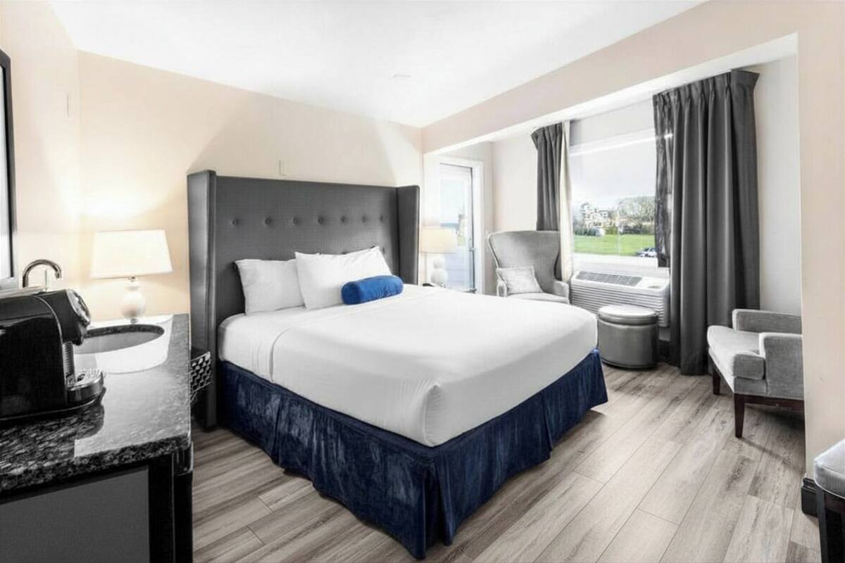 A hotel room with a large bed, a desk with a lamp, a chair, a window with curtains, and a view of the outdoors.