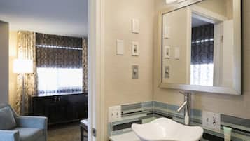 Un baño de hotel con un lavamanos grande, un espejo y una silla en la habitación contigua.