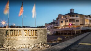 A hotel named "Aqua Blue" with a stone sign, multiple flags, and a multi-story building with balconies and lights. - Aqua Blue Hotel (Narragansett)