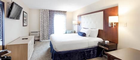 Habitación de hotel con cama, mesita de noche, lámpara, televisor y escritorio con silla.
