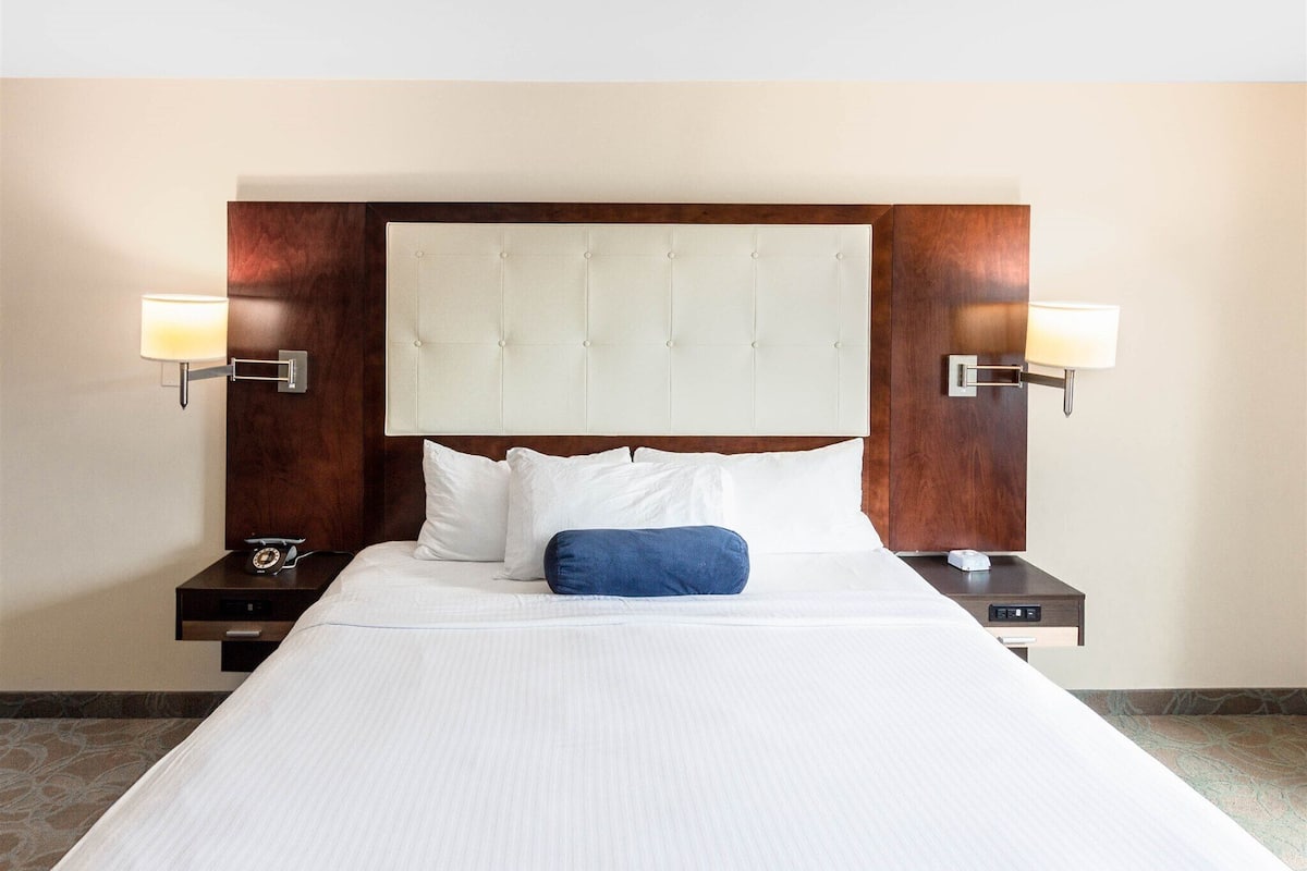 A hotel room with a large bed, two bedside tables, a wooden headboard, and wall-mounted lamps.