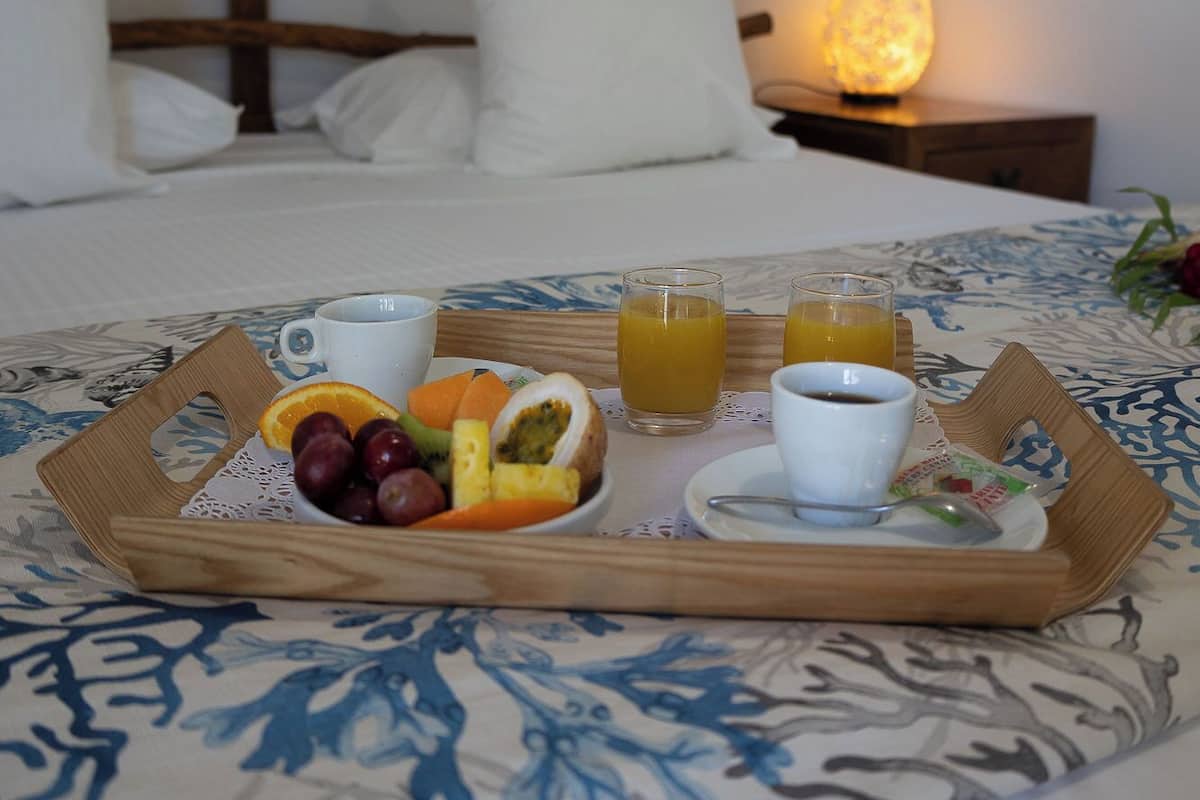 Ein ordentlich gedeckter Frühstückswagen auf einem Bett mit floralem Überwurf, einem Holzkopfteil und einer Nachttischlampe.