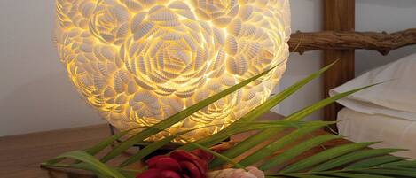 A decorative light fixture with a textured surface, placed on a wooden table with green leaves and red flowers.