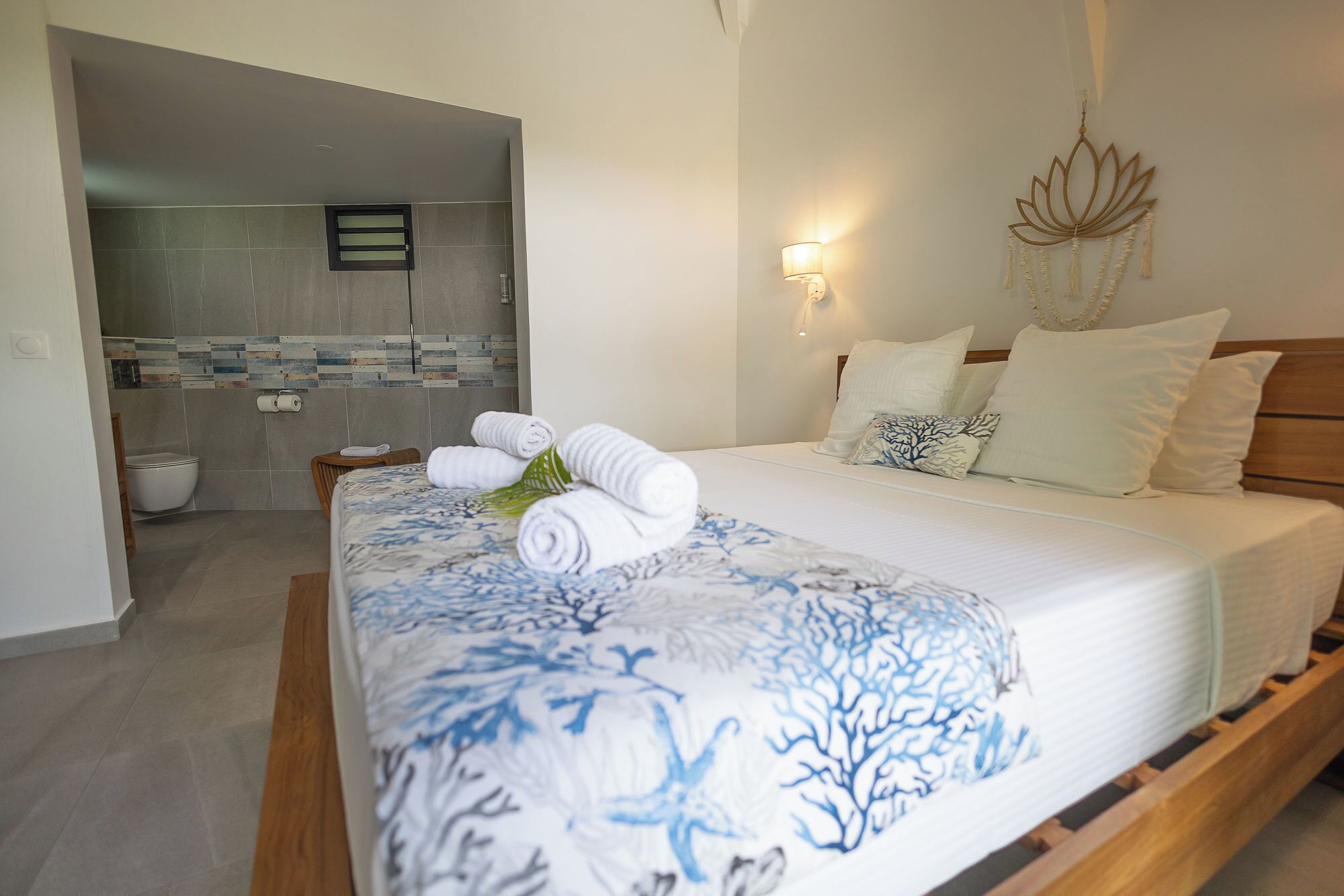 A hotel room with a bed, a nightstand, a wall-mounted light, and a bathroom visible through an open door.