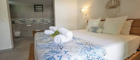 A hotel room with a bed, a nightstand, a wall-mounted light, and a bathroom visible through an open door.
