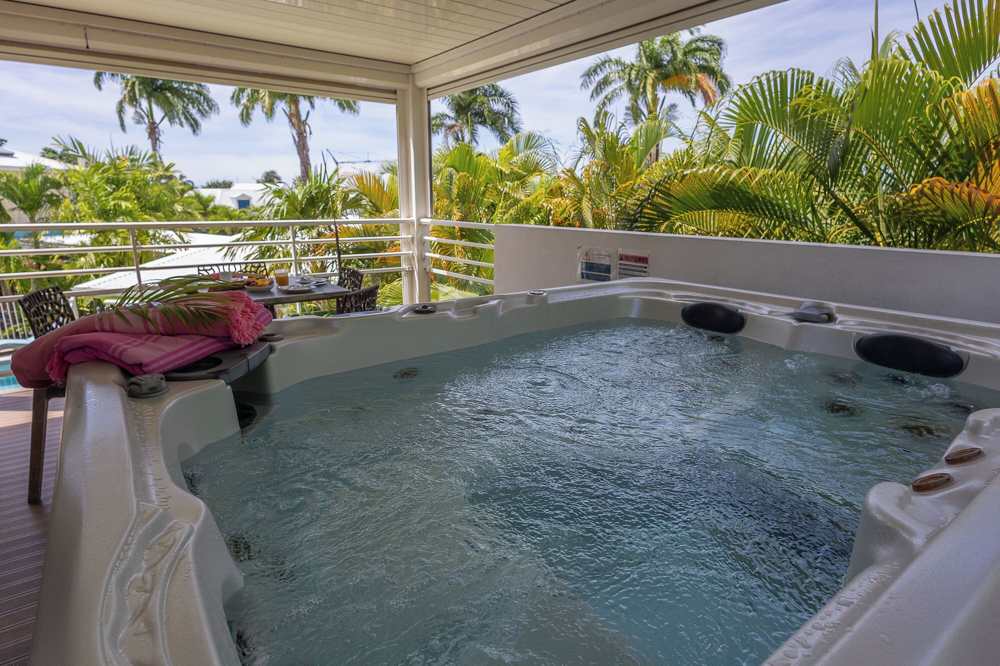 Ein Whirlpool mit Blick auf Palmen und einer überdachten Terrasse.