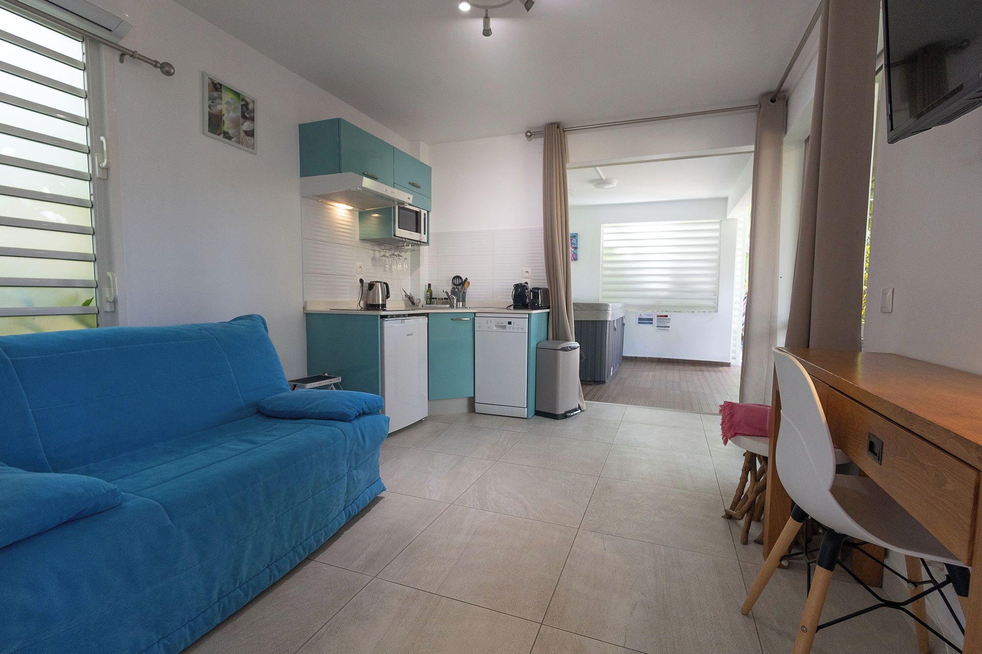 A compact living space with a kitchenette, a blue sofa, a dining area with a table and chairs, and a TV mounted on the wall.