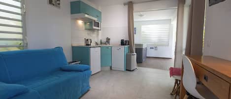 A compact living space with a kitchenette, a blue sofa, a dining area with a table and chairs, and a TV mounted on the wall.