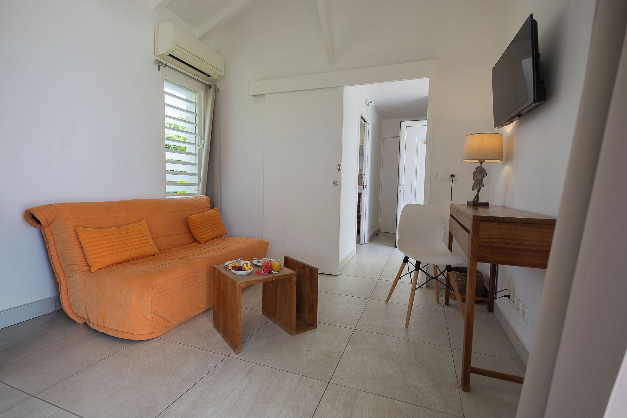 Een kamer met een bank, een kleintje tafeltje met fruit, een lamp en een televisie.