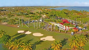 A golf course with palm trees, a clubhouse, and a view of the ocean. - Majesty Palm (Saint-François)