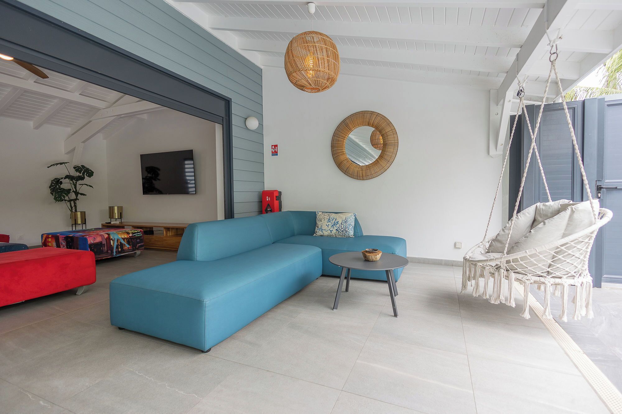 A modern living room with a blue sectional sofa, a round coffee table, a hanging chair, and a large mirror on the wall.